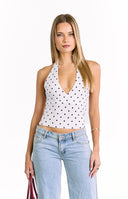 A white halter-style crop top with a black polka dot pattern and a deep, plunging V-neckline. The top has a wrap-style front.