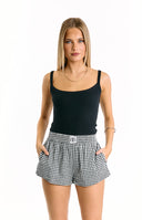 White ribbed scoop-neck tank top paired with black and white gingham print shorts featuring an elastic waistband. A black shoulder bag is worn.