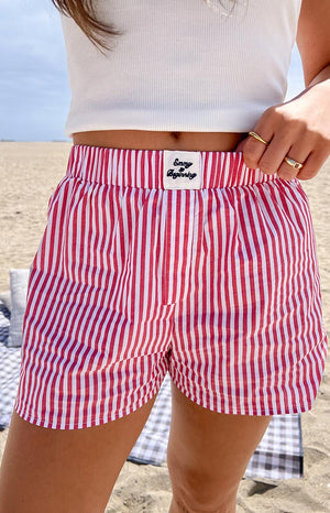 Girl is shown in red and white striped shorts with a visible "Emmy x Beginning" label on the front of the waistband- complemented by a white tank top.