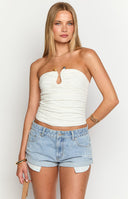 Model is wearing a white strapless top with a metal bar structuring the bust. Top has an orange stone detailing. Model is wearing gold jewellery and lightwash denim.
