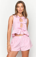 Close up of girl in pink gingham shorts and matching top, holding a drink.